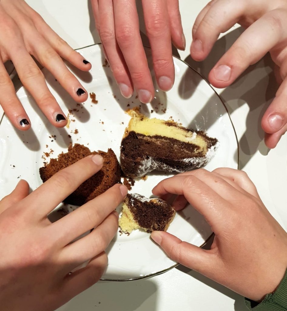 Fünf Hände greifen nach Kuchen, der auf einem Teller liegt.