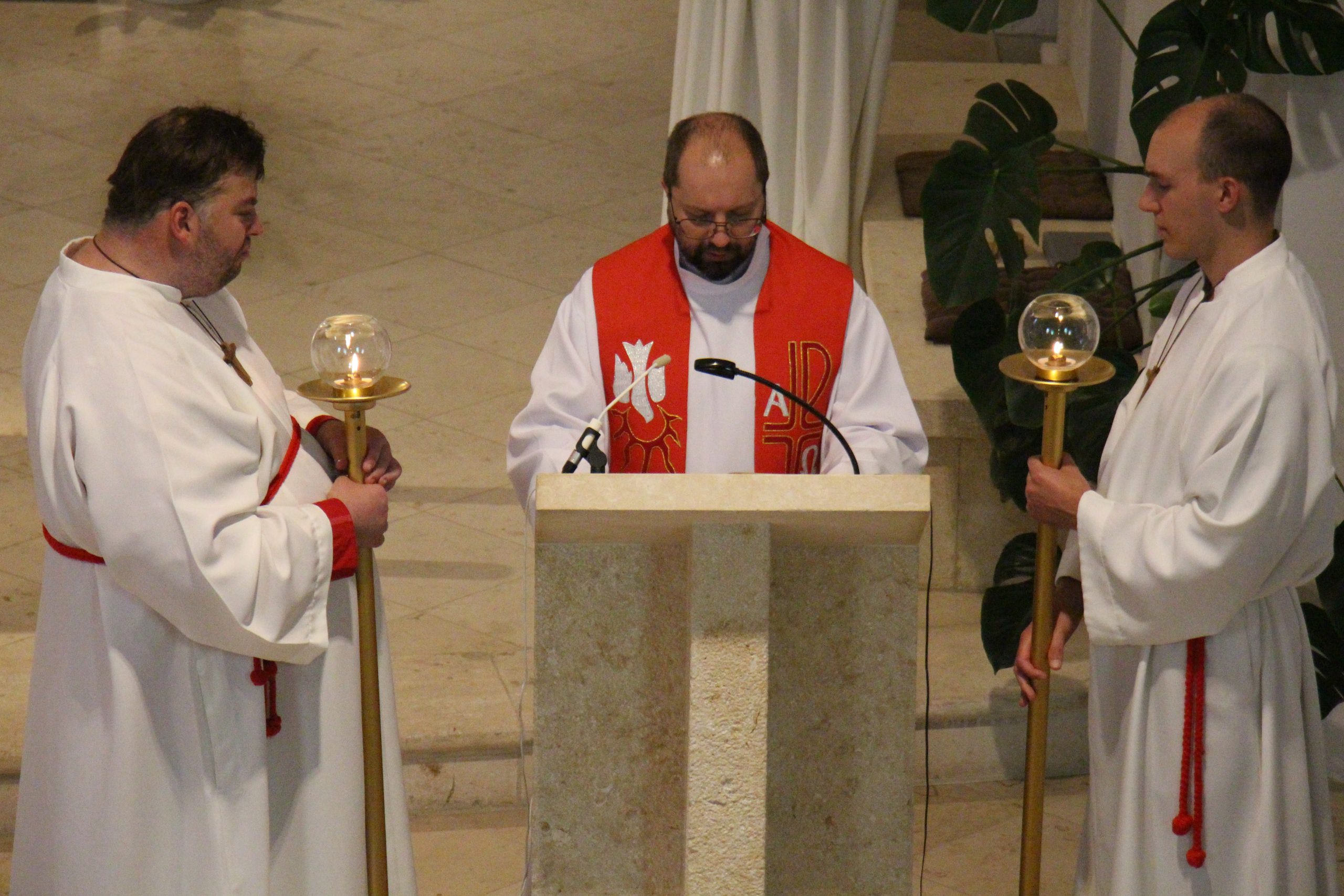 Pfarrvikar Marcin steht am Ambo, zwei Ministranten links und rechts halten Kerzen.