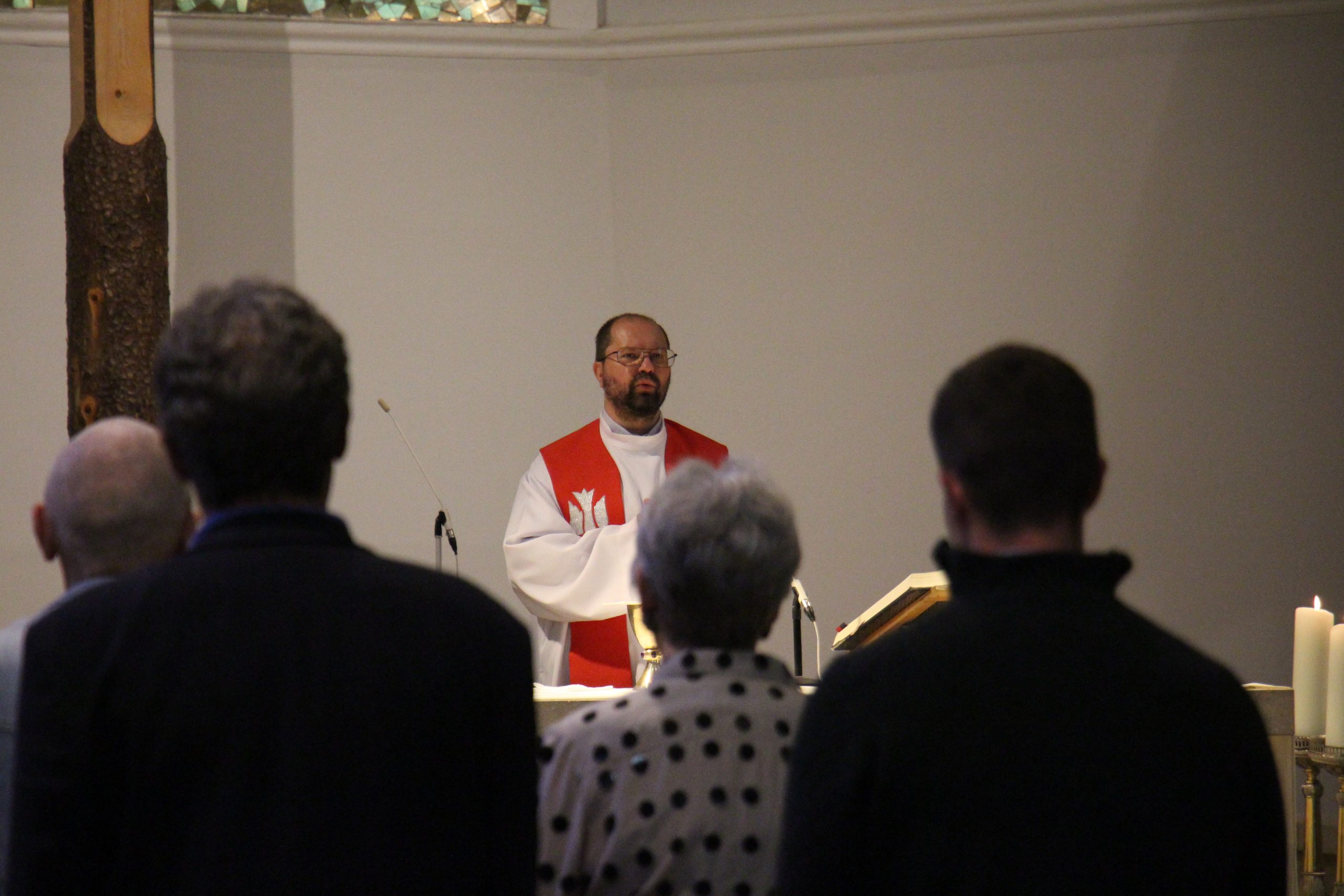 Pfarrvikar Marcin steht am Altar und spricht; Messbesucher in den Reihen.